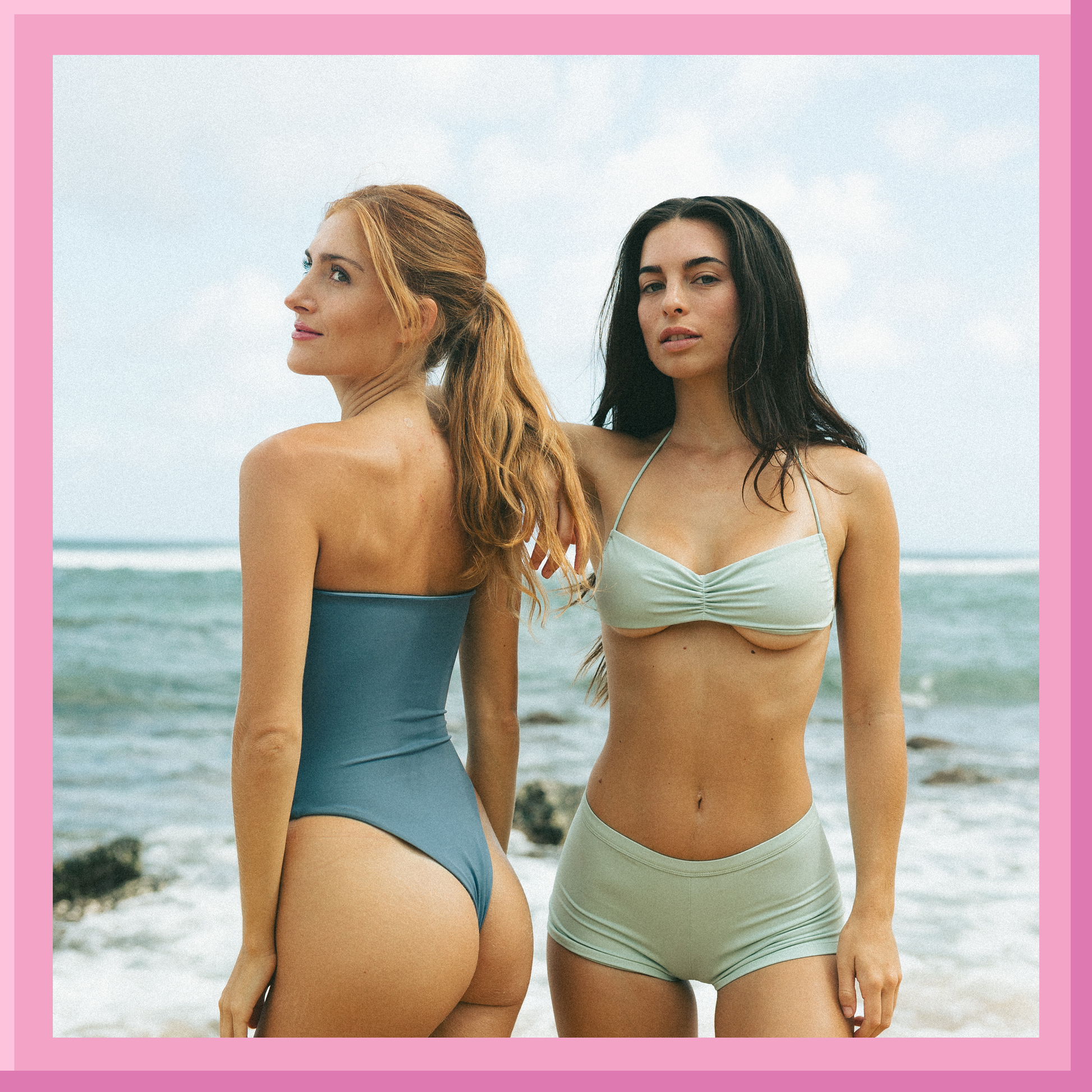 Two women in swimsuits standing on a beach with a pink border.
