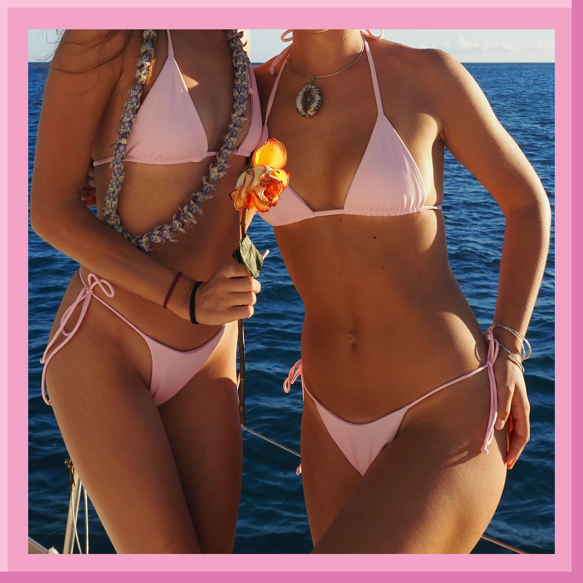 Two women in pink bikinis standing by the ocean with a pink border.